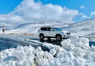 white car parked on a road with piles of snow on the side and snowy hills in the background, part of a tour from Marrakech to see the Atlas Mountains in winter.