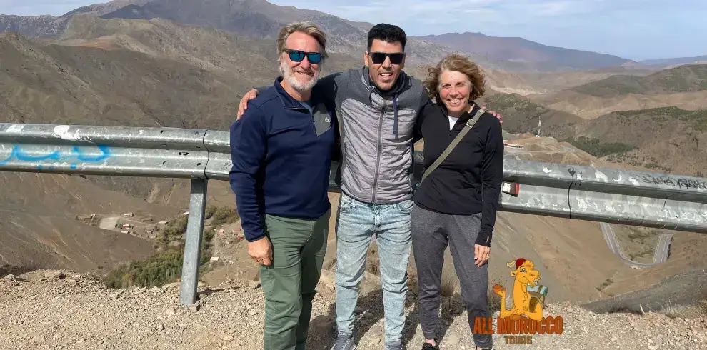 guide stands with two tourists against the background of rolling mountains on the Tizi n Tichka pass a part of their 3 days Sahara Desert tour from Marrakech.