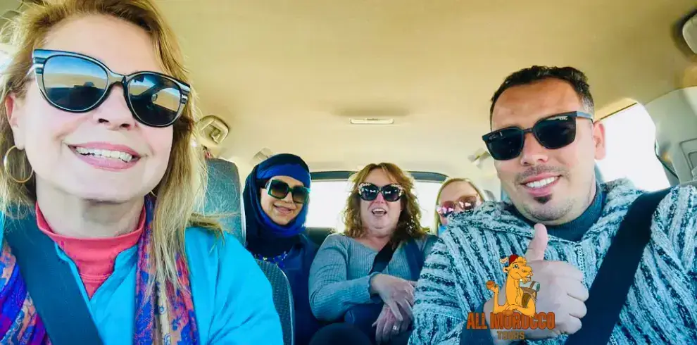 group of five cheerful tourists wearing sunglasses, giving thumbs up in a car, during an 8 days tour from Casablanca to Marrakech.