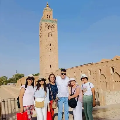 A group of tourists smiling in front of the Kutubiyya Mosque a significant landmark in the tours category Marrakech on a sunny day