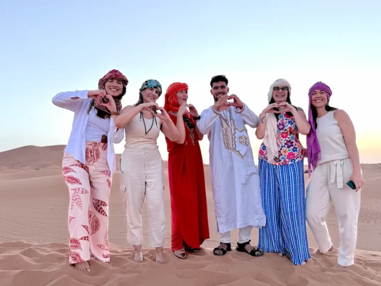 Six travelers wearing traditional clothing and posing together on Sahara sand dunes.