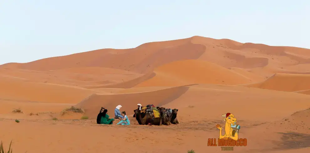 Travelers resting with camels among the sand dunes of the Merzouga Sahara Desert